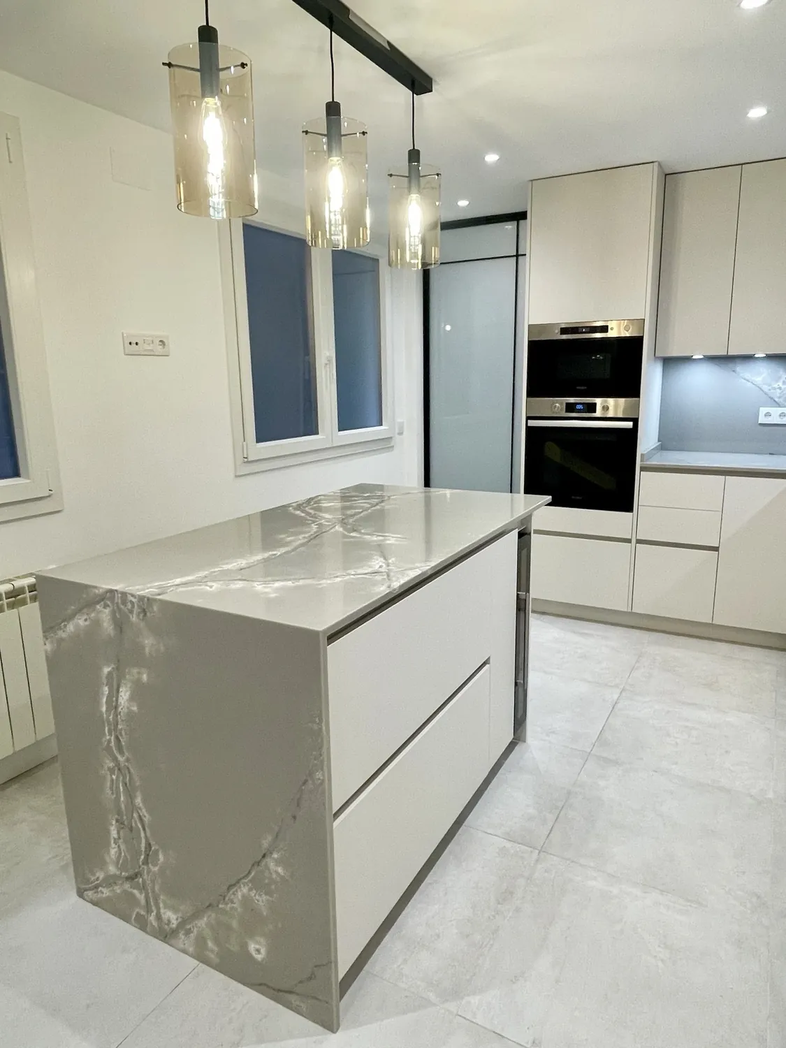Cocina con isla de acabado efecto mármol y lámparas colgantes, vivienda en atocha