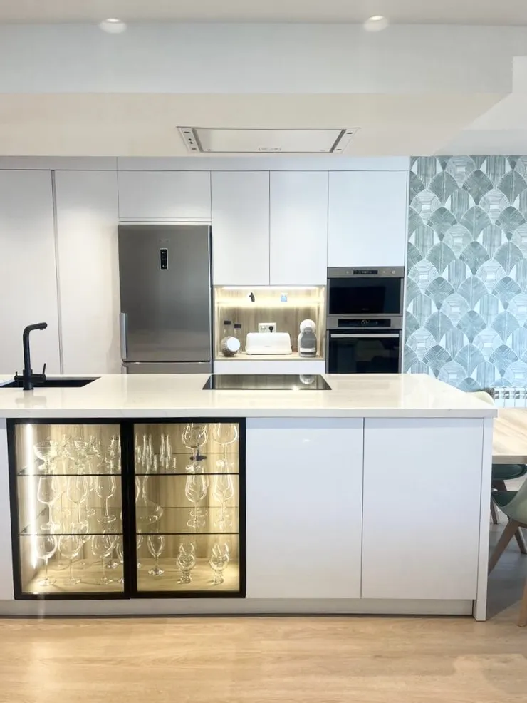 Cocina blanca con isla, vitrina iluminada y papel pintado geométrico, vivienda en montecarmelo