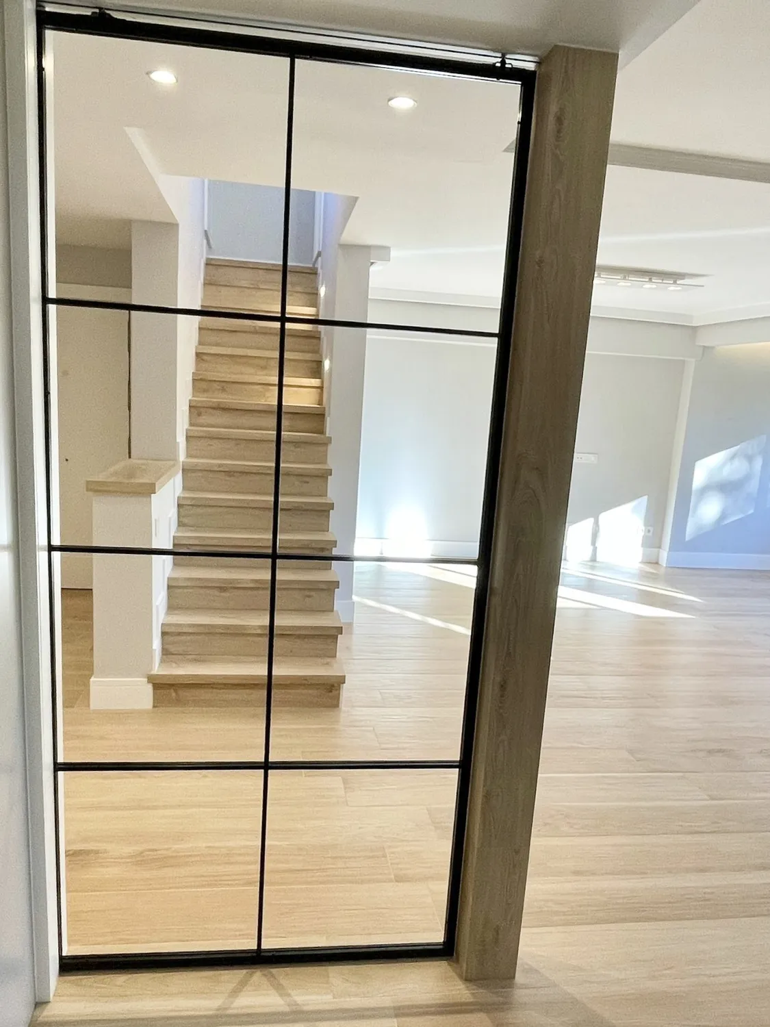 Cerramiento de vidrio con perfilería negra frente a la escalera de madera, vivienda en La Moraleja