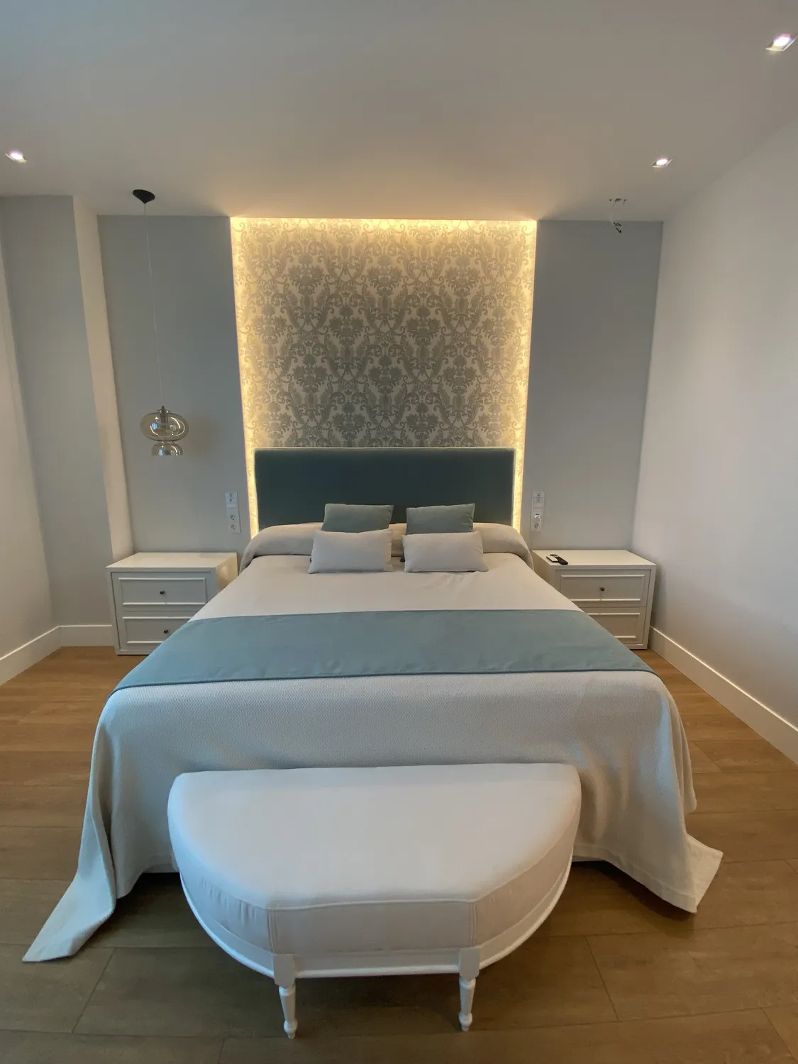 Dormitorio con cabecero azul tapizado e iluminación indirecta, vivienda en Pintor Rosales